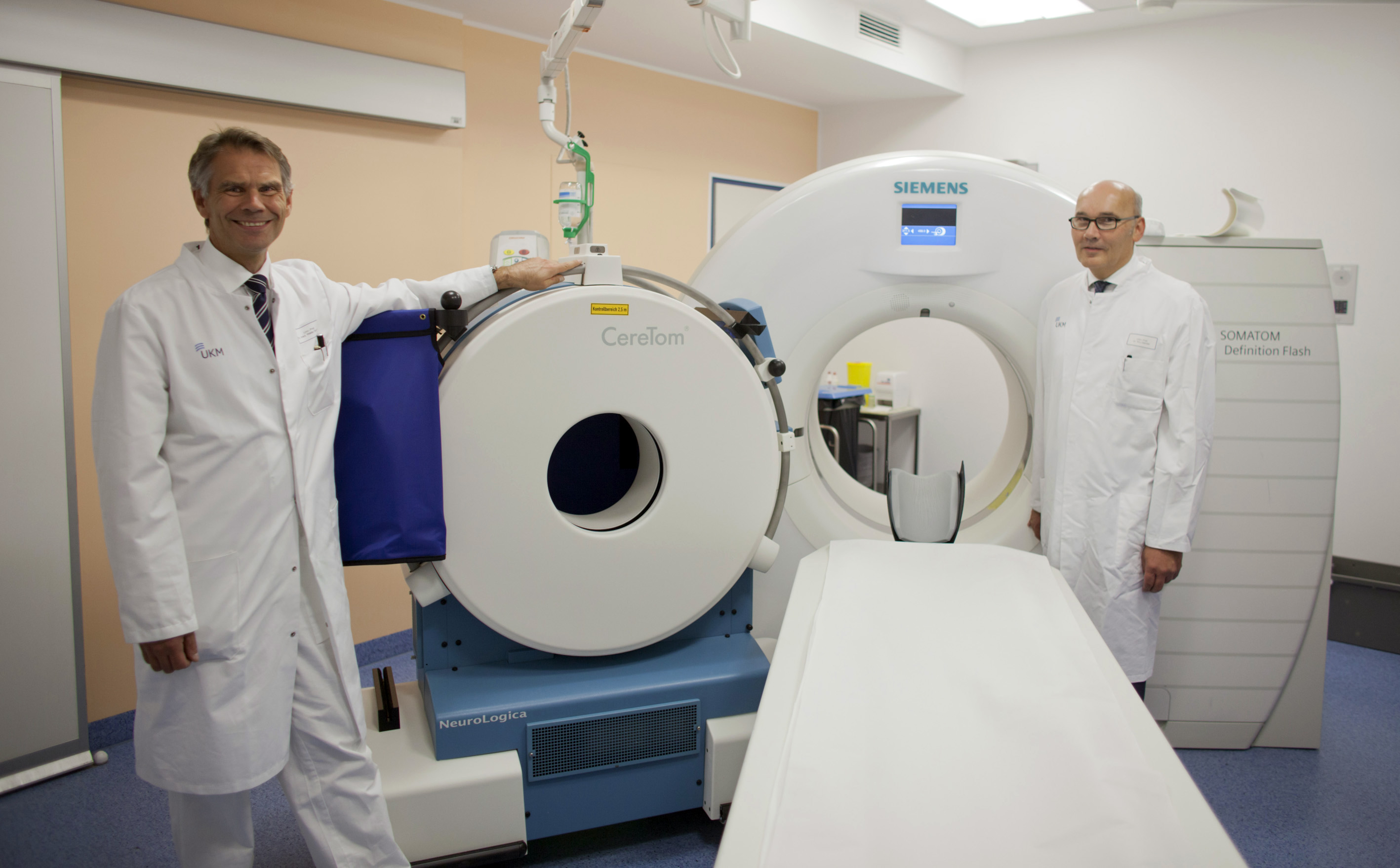 Prof. Dr. Walter Stummer (links) und Prof. Dr. Walter Heindel zeigen den Größenunterschied zwischen dem voll-mobilen CT und einem fest installierten Gerät.